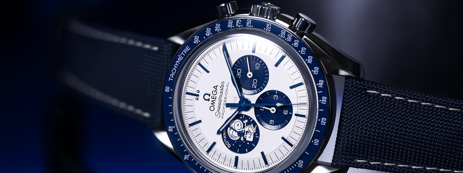 Speedmaster Silver Snoopy Award 50th Anniversary schräg von vorn auf dunkler, spiegelnder Fläche mit blauem Licht